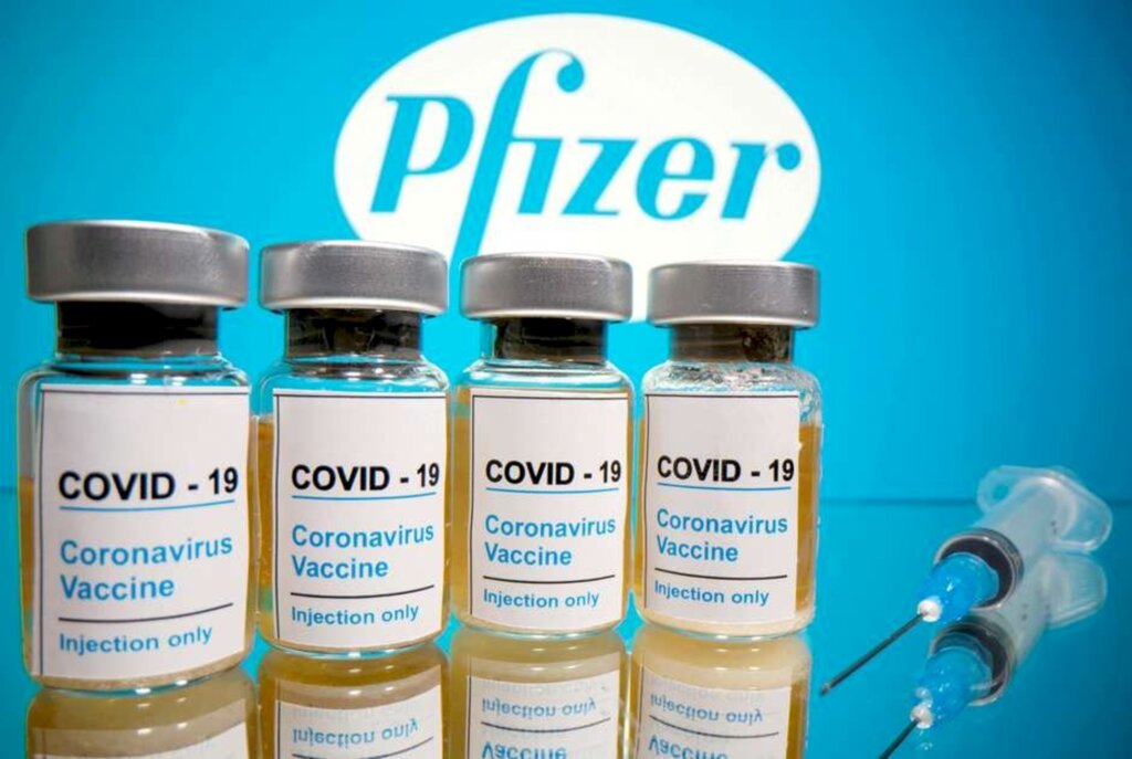 Dado Ruvic - Seringa e frascos rotulados como de vacina para Covid-19 em frente a logo da Pfizer em foto de ilustração