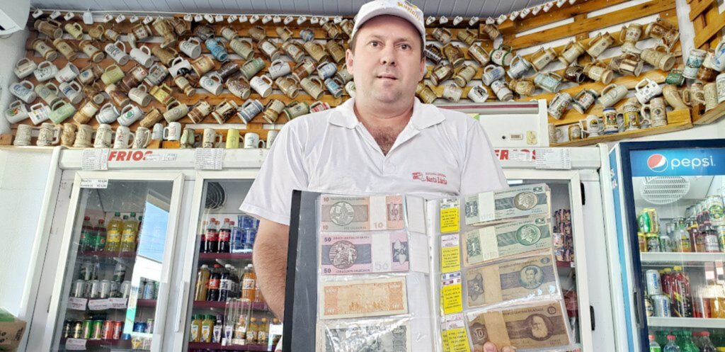  - Adriano Moacir Bauermann segurando parte da coleção de cédulas (dinheiro) e de moedas, também no detalhe copos de chope de porcelana. Dia 20 de março de 2020.